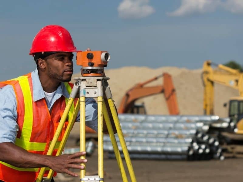 Surveyor reviewing site plans and measuring an older commercial property during an ALTA survey before purchase.